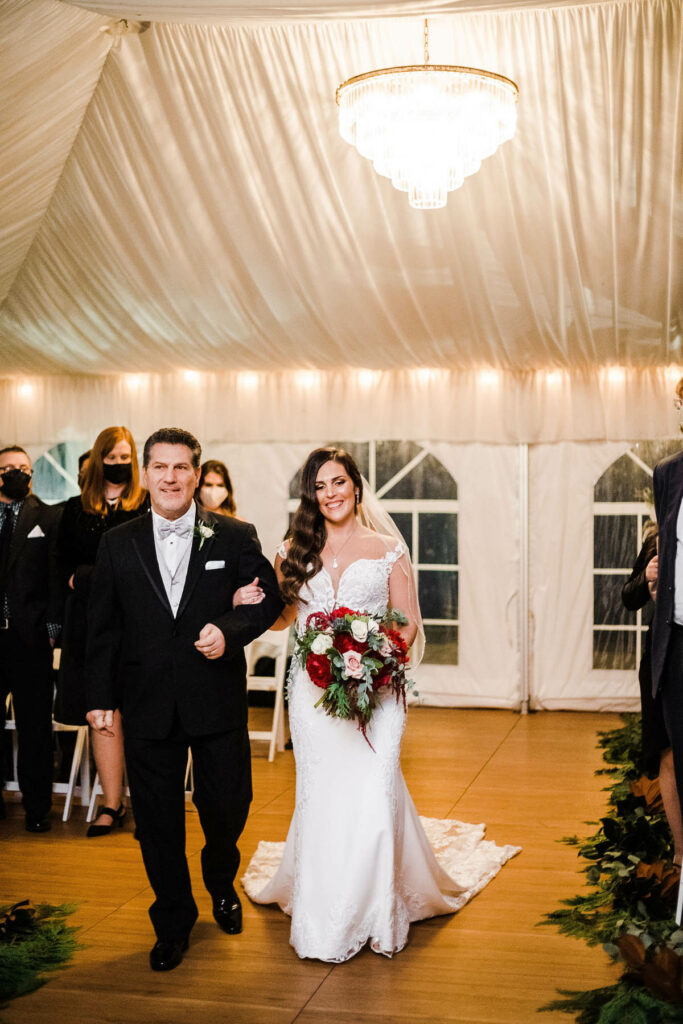 Father and bride walking aisle in in white tent at night